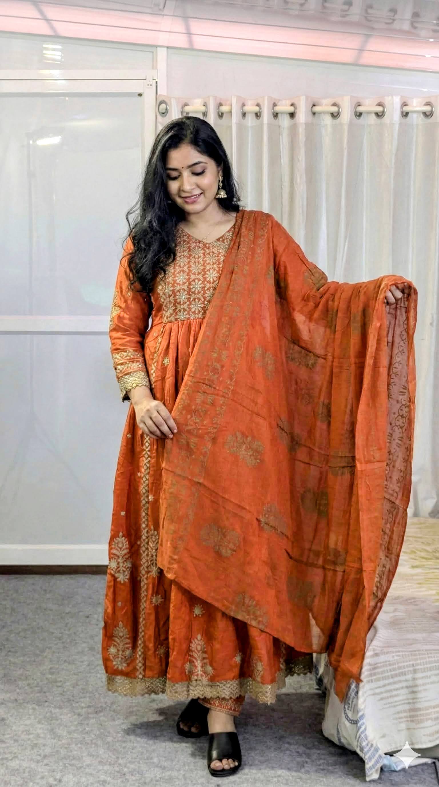 Woman wearing an orange traditional outfit with a dupatta in a neutral indoor setting
