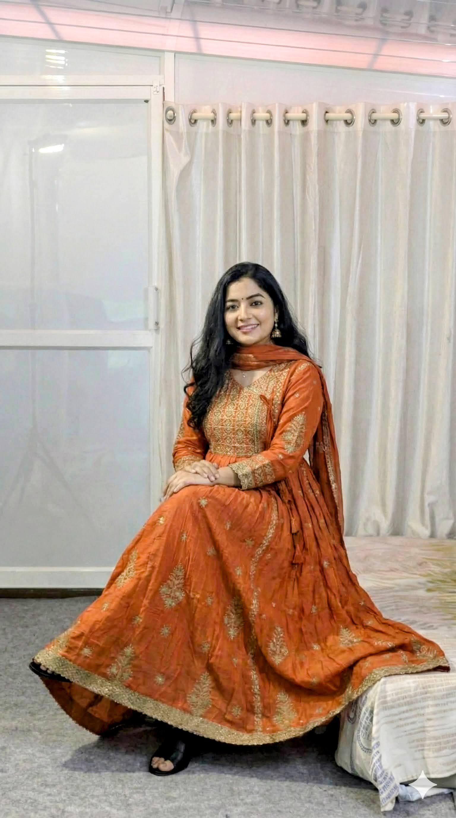Woman in an orange traditional outfit sitting on a white chair indoors.
